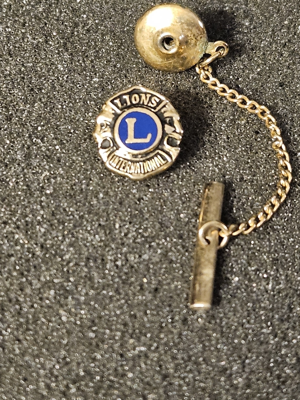 A vintage gold-tone Lions Club International tie tack and lapel pin with a chain